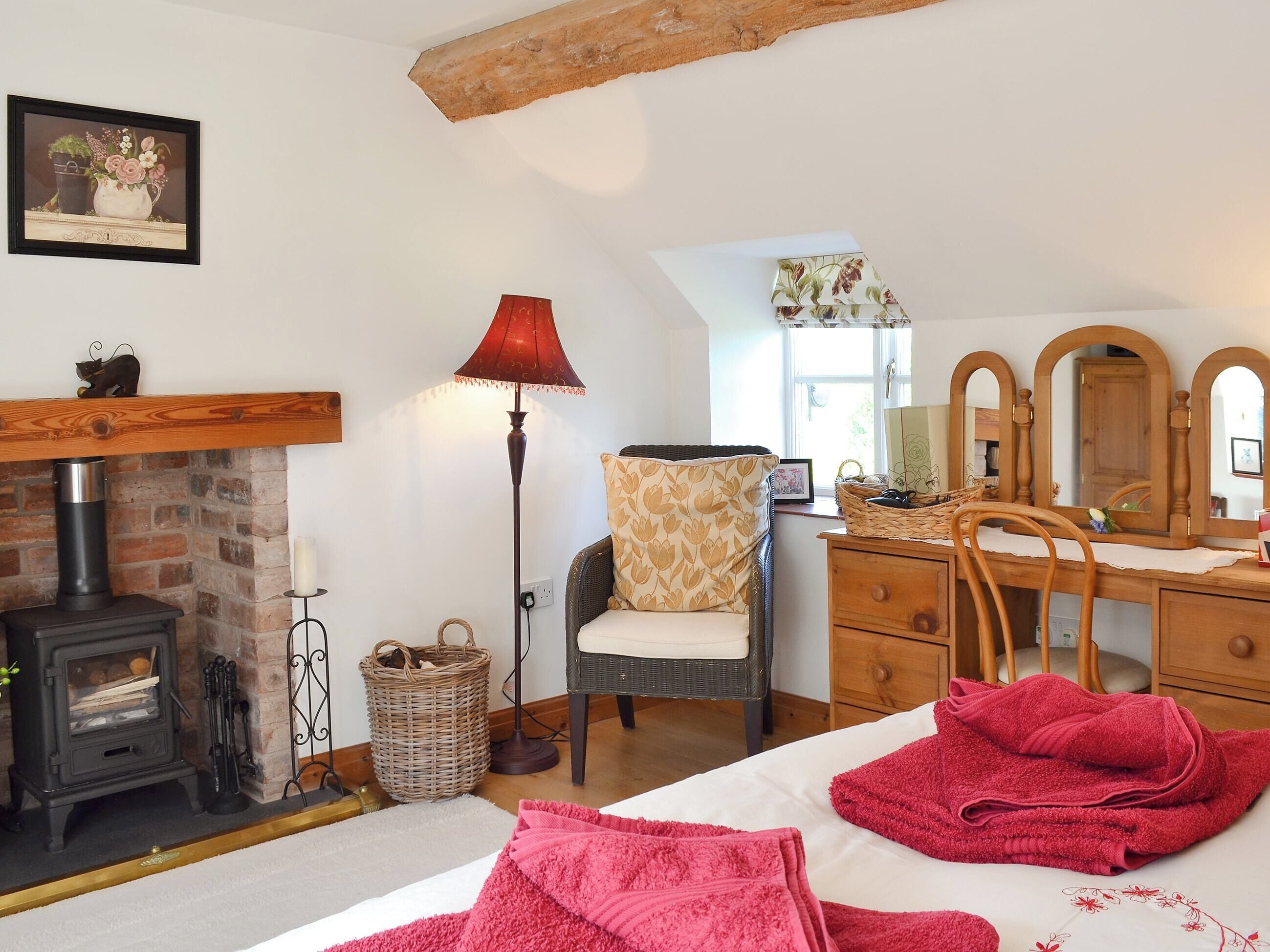 Un dormitorio acogedor con chimenea, un aparador de madera, una silla y una cama con toallas rojas.