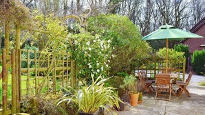 Un jardin agrémenté d’une pergola en bois, de plantes en pot et d’une table avec des chaises placée sous un parasol vert.