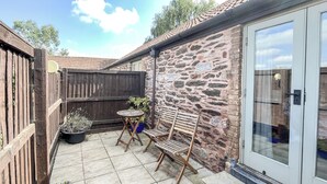 A patio with a stone floor, wooden furniture, and a stone wall. - 1 bedroom accommodation in North Newton (North Newton)
