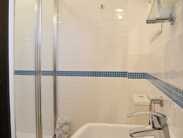 Une salle de bain dotée d’une douche à parois de verre, d’une baignoire blanche et d’une bande décorative aux carreaux bleus.