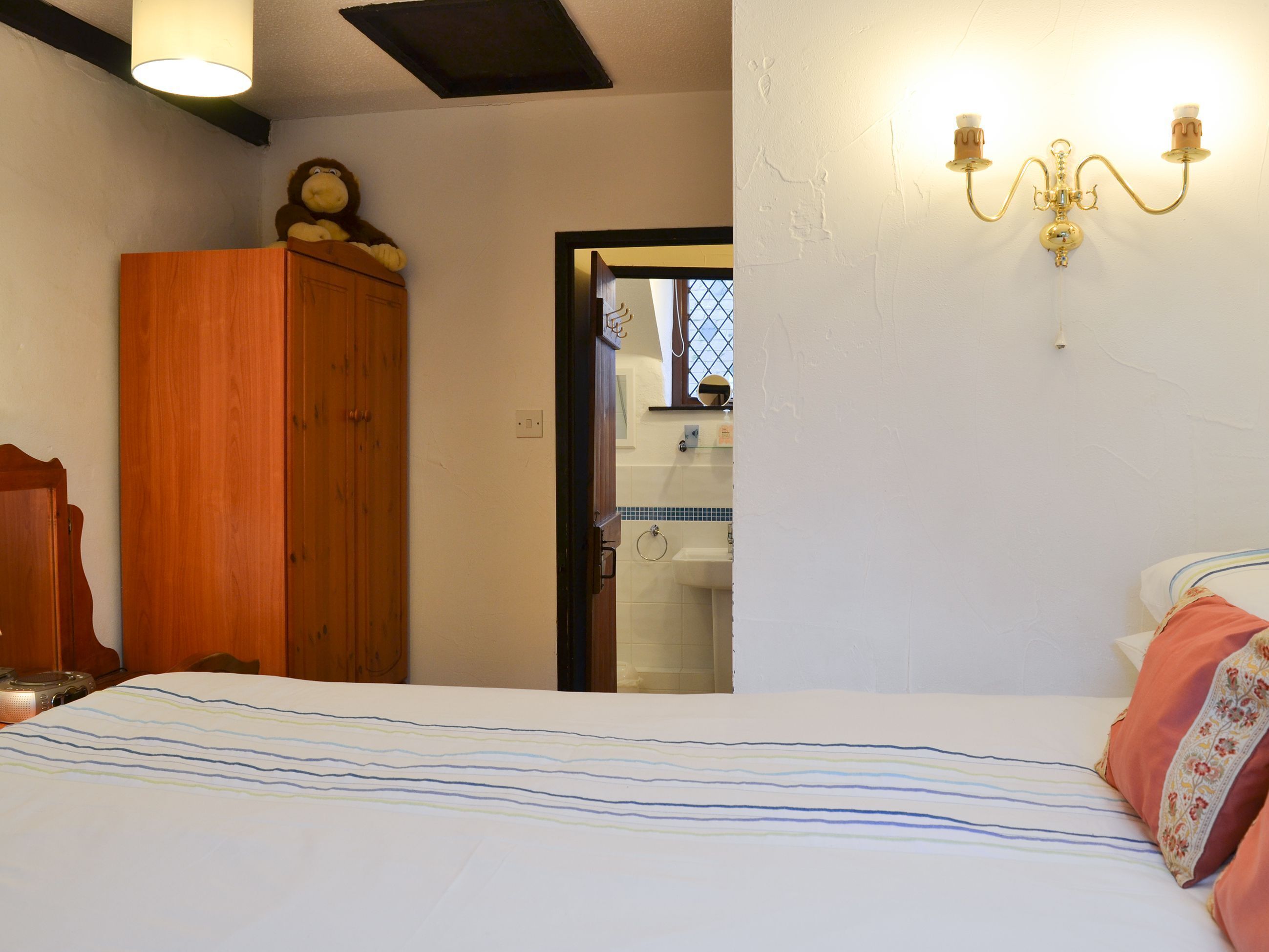 Un dormitorio con cama, armario de madera y baño visible a través de una puerta abierta.