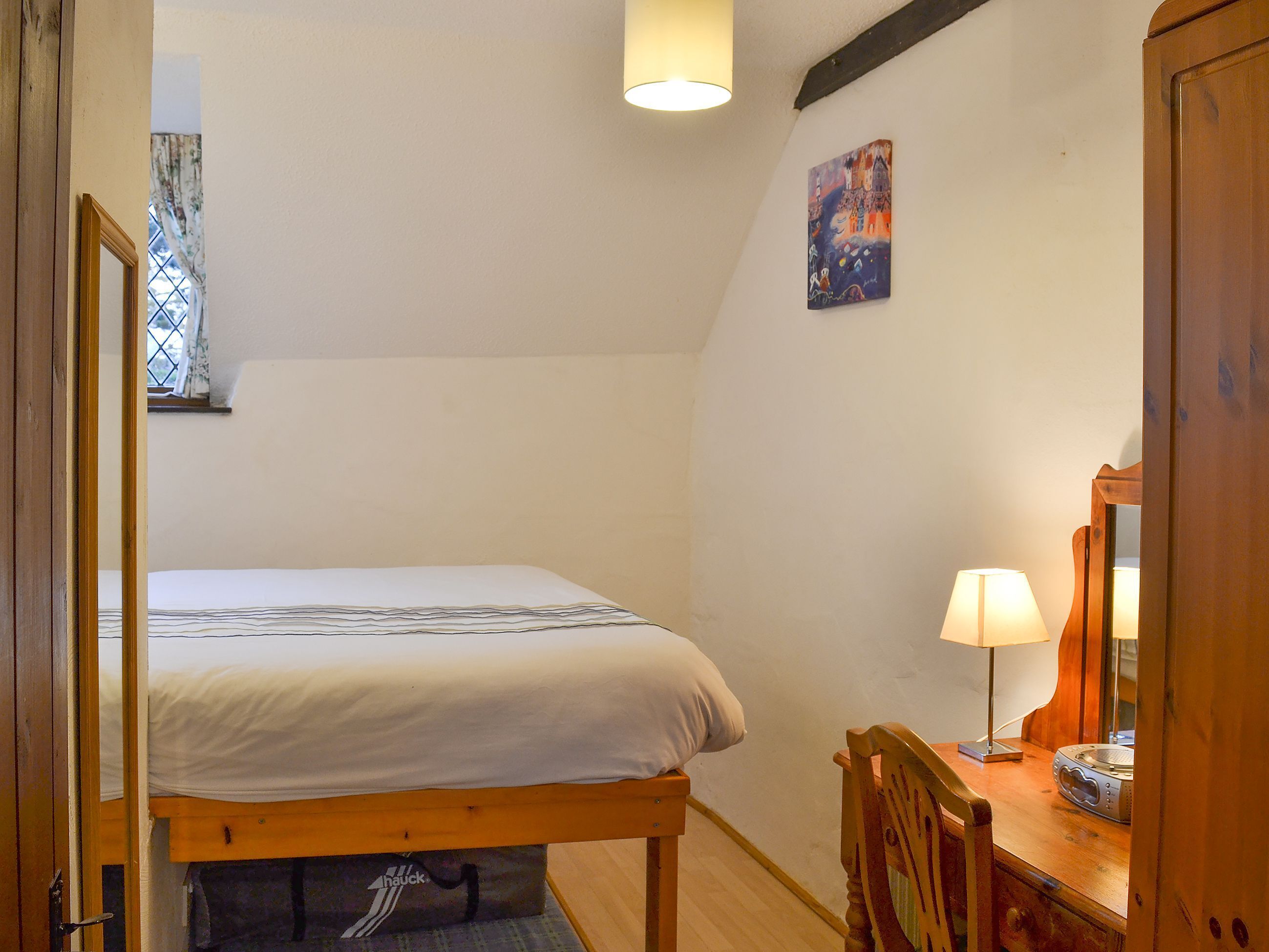 A bedroom with a bed, a desk with a lamp, a chair, and a painting on the wall.