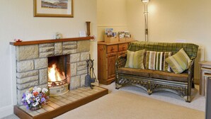 A cozy living room with a stone fireplace, a green plaid sofa, and a lamp.
