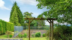 A garden with a wooden pergola, stone wall, and various plants.
