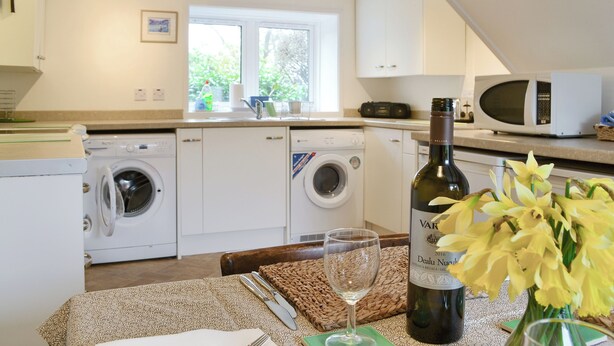 A kitchen with a washing machine, a microwave, and a wine bottle on the counter.