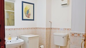 Een badkamer met een wastafel, toilet en douche. Er hangt een lijst met een afbeelding aan de muur.
