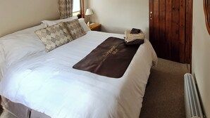 Een net opgemaakt bed met een bagagemat, een houten garderobe, een nachtkastje met een lamp en een lijst met een foto aan de muur.
