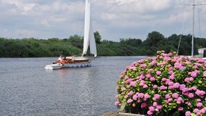 Een zeilboot op een rustig wateroppervlak met een aangemeerd boot in de buurt.