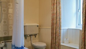 Une salle de bain avec des toilettes, une douche avec un rideau et une fenêtre agrémentée de rideaux à motifs floraux.