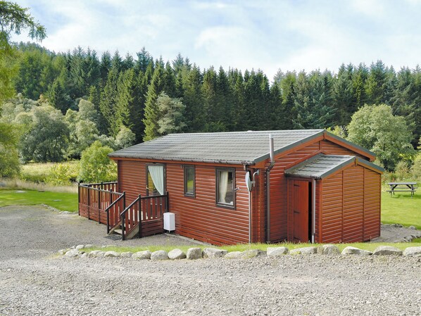 Een klein houten huisje met een veranda en een picknicktafel, gelegen in een bebost gebied.