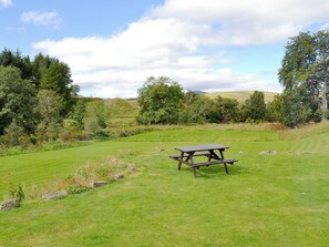 Een picknicktafel in een grasveld, met bomen en heuvels op de achtergrond.