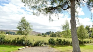 Un sendero de grava que lleva a una zona cubierta de césped, con árboles y colinas al fondo.