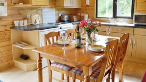 Cocina de cabaña de madera con mesa para dos, estufa y ventana con vista a árboles.