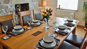 A dining table set with plates, glasses, and cutlery, flanked by chairs, in a room with stone walls and a window. - 2 bedroom accommodation in Trefor, near Caernarfon (Trefor, near Caernarfon)