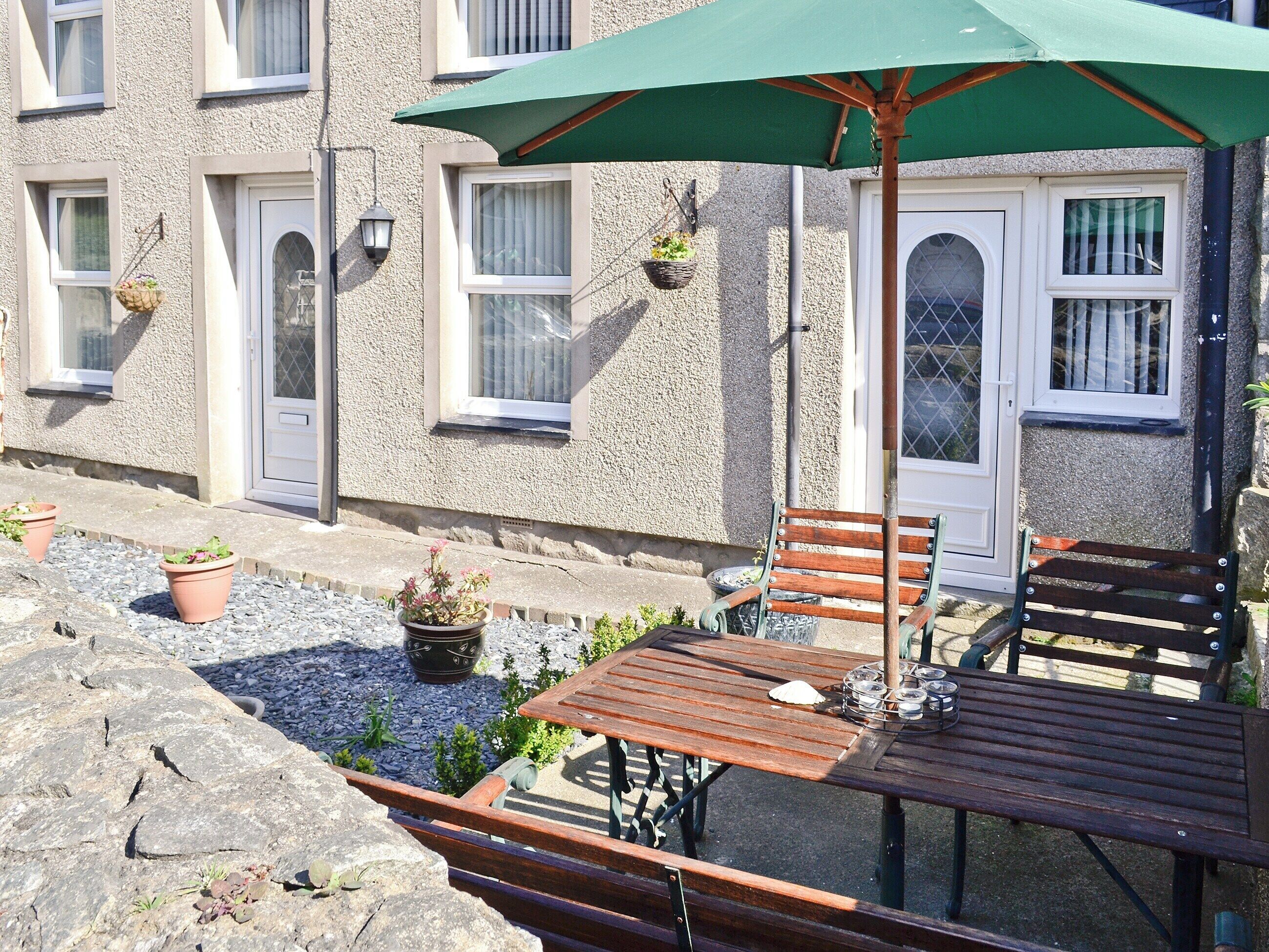 An outdoor seating area with a wooden table and benches, a green umbrella, and potted plants.