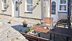 An outdoor seating area with a wooden table and benches, a green umbrella, and potted plants. - 2 bedroom accommodation in Trefor, near Caernarfon (Trefor, near Caernarfon)