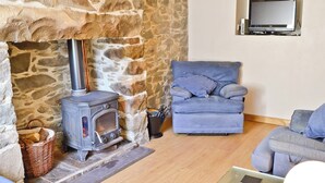 A cozy living room with a stone fireplace, a blue sofa, and a television mounted on the wall. - 2 bedroom accommodation in Trefor, near Caernarfon (Trefor, near Caernarfon)