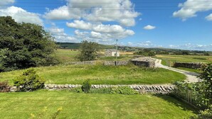 Un paysage rural avec un mur de pierres, un bâtiment en pierre et un chemin de terre menant à une porte.