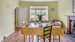Une salle à manger avec une nappe à carreaux, des chaises, un vase de fleurs et une vue sur l’extérieur par une fenêtre.