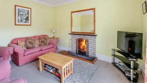 Un salon avec un canapé rose, une cheminée, un téléviseur et une petite table en bois.