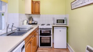 Une cuisine de taille réduite, dotée d’appareils électroménagers blancs, de meubles en bois et d’un dosseret carrelé.