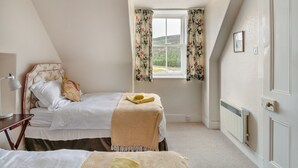 Une chambre avec deux lits, une fenêtre ornée de rideaux à motifs floraux, un radiateur et une porte.