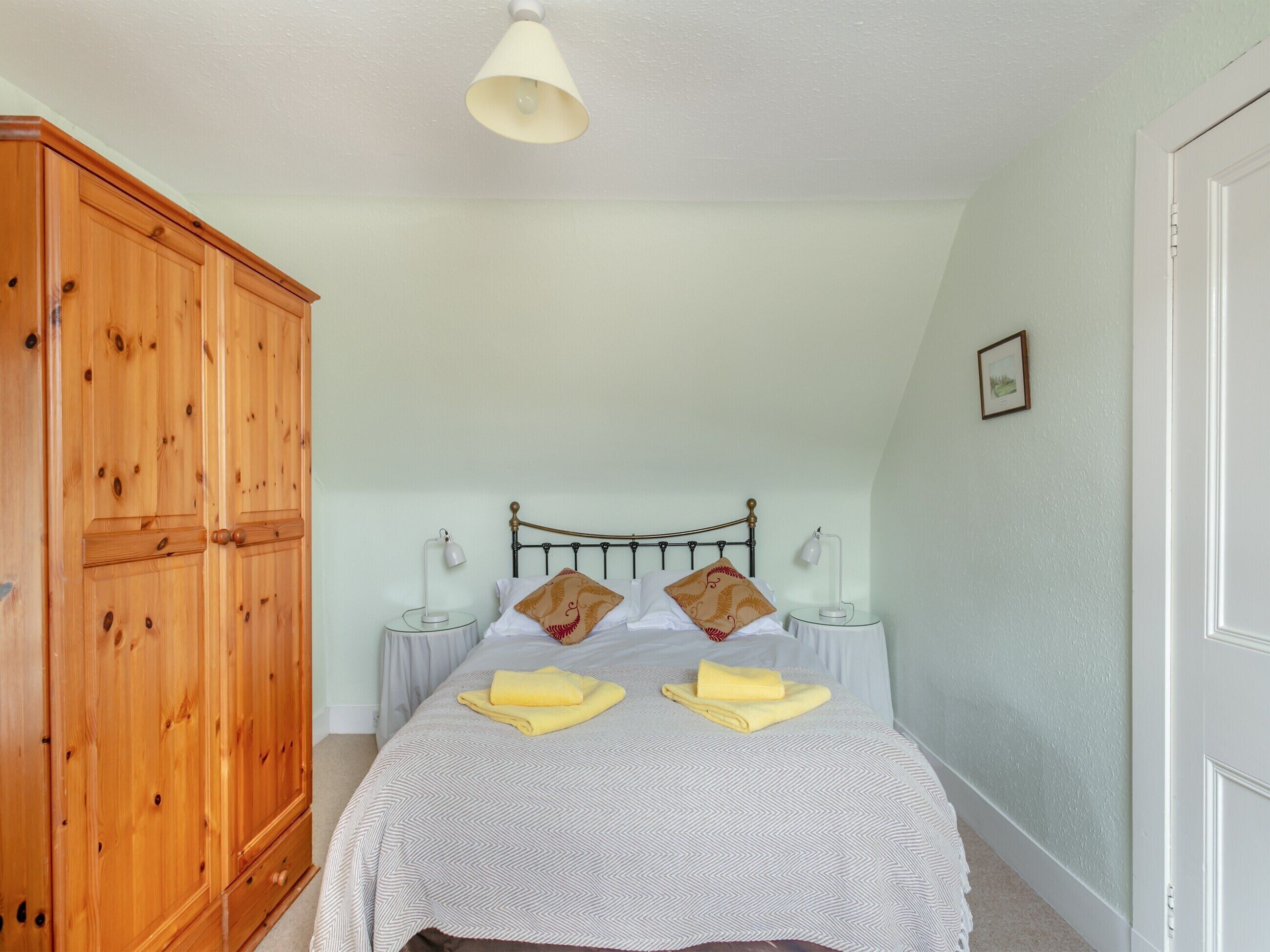 Une chambre à coucher avec un lit, deux lampes de chevet, une armoire en bois et un luminaire au plafond.