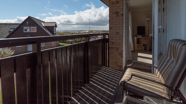 Un balcon avec une balustrade en bois, une chaise et une vue sur une maison et le paysage environnant.