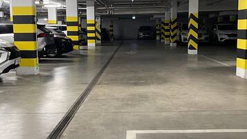 En parkeringskælder med flere etager, tydelige pile på gulvet, gule og sorte sikkerhedsværn samt et ventilationssystem i loftet.