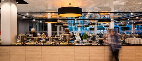 Un restaurante moderno con una barra central que exhibe diversos platos, iluminación ambiental y un diseño de techo contemporáneo.