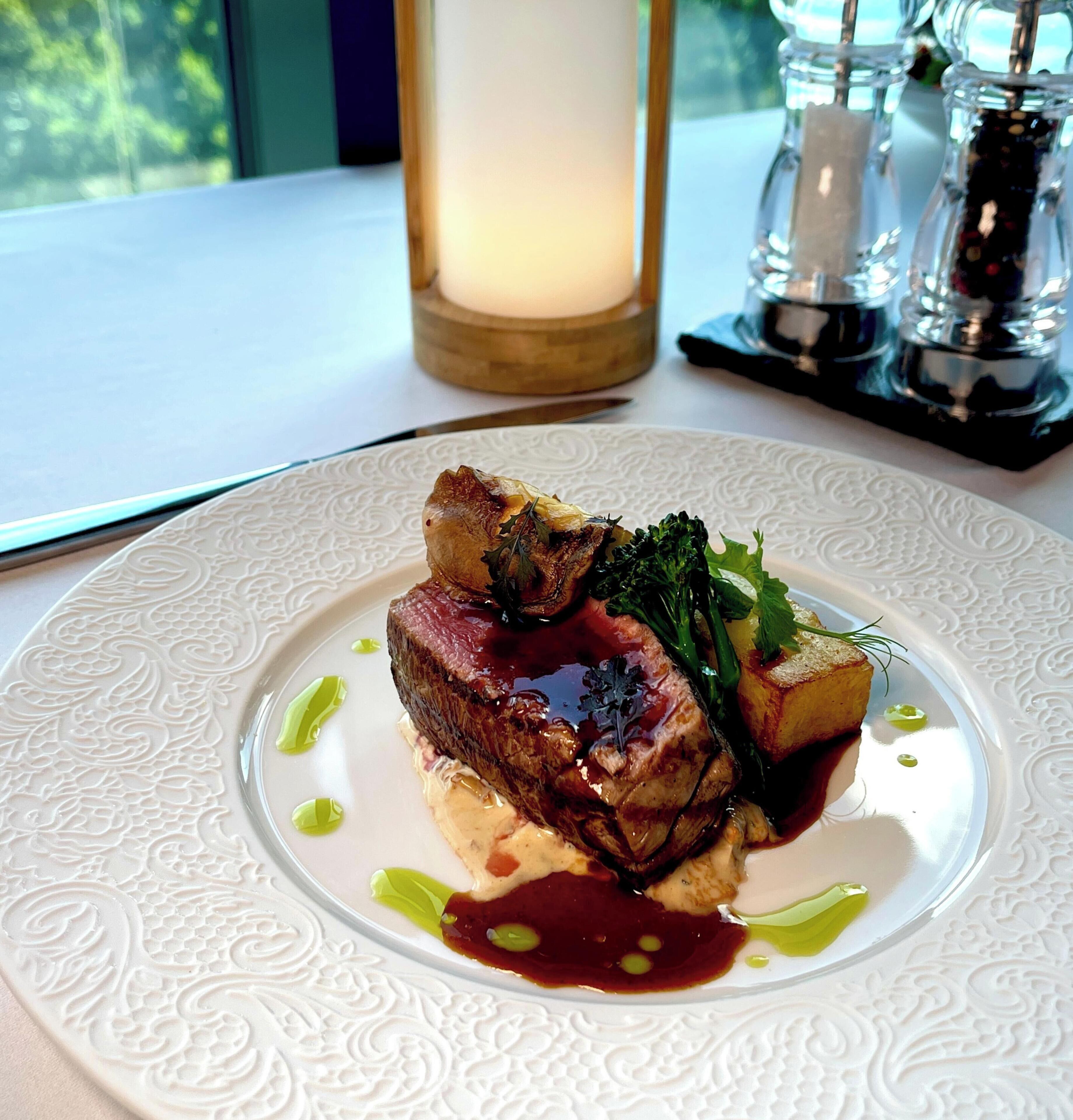 Un plato de comida con carne, verduras y salsa sobre un plato blanco con textura.