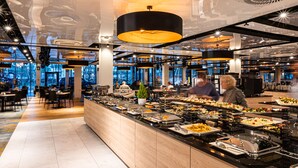 A buffet area with various food options, a seating area with tables and chairs, and a modern interior design with large windows and ceiling lights. - Hamilton Conference Hotel Spa & Wellness (Swinoujscie)