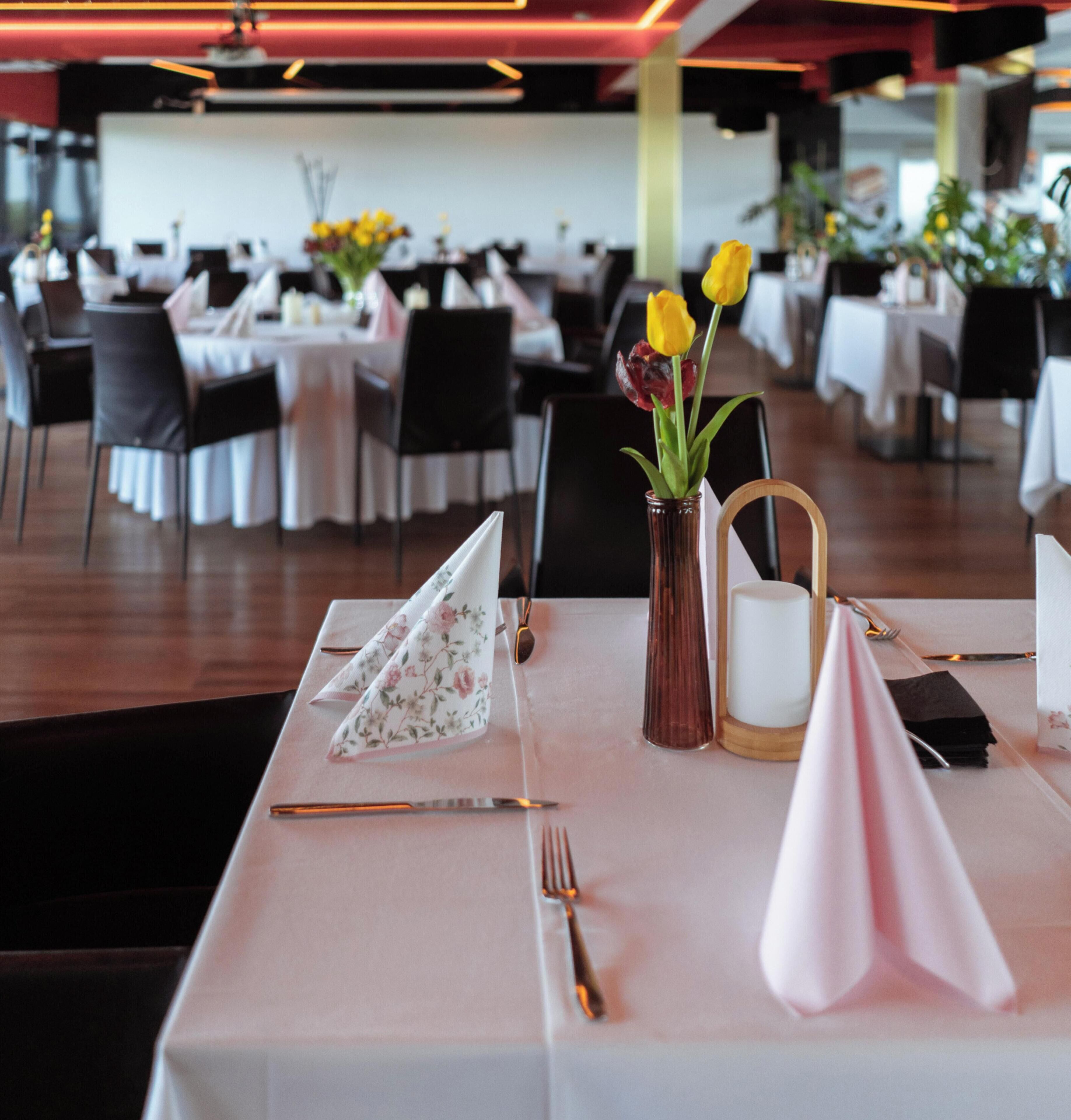 A dining table set with a vase of flowers, a candle, and folded napkins.
