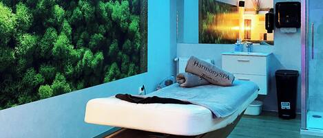 A modern bedroom with a bed, a bedside table, a mirror, a wall-mounted heater, and a trash bin.