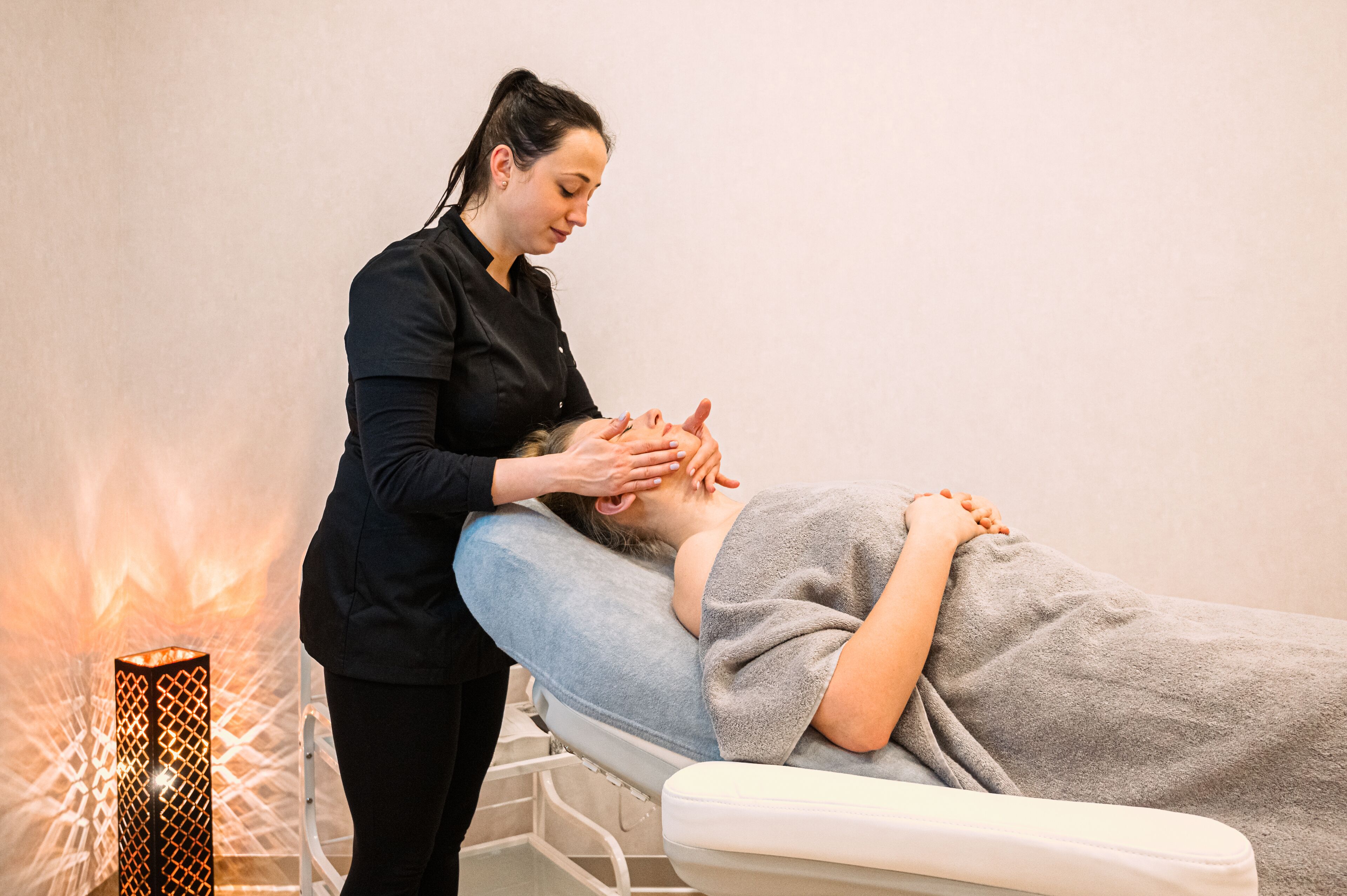 A person receiving a massage on a massage table in a room with a geometric light fixture.