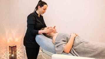 A person receiving a massage on a massage table in a room with a geometric light fixture.