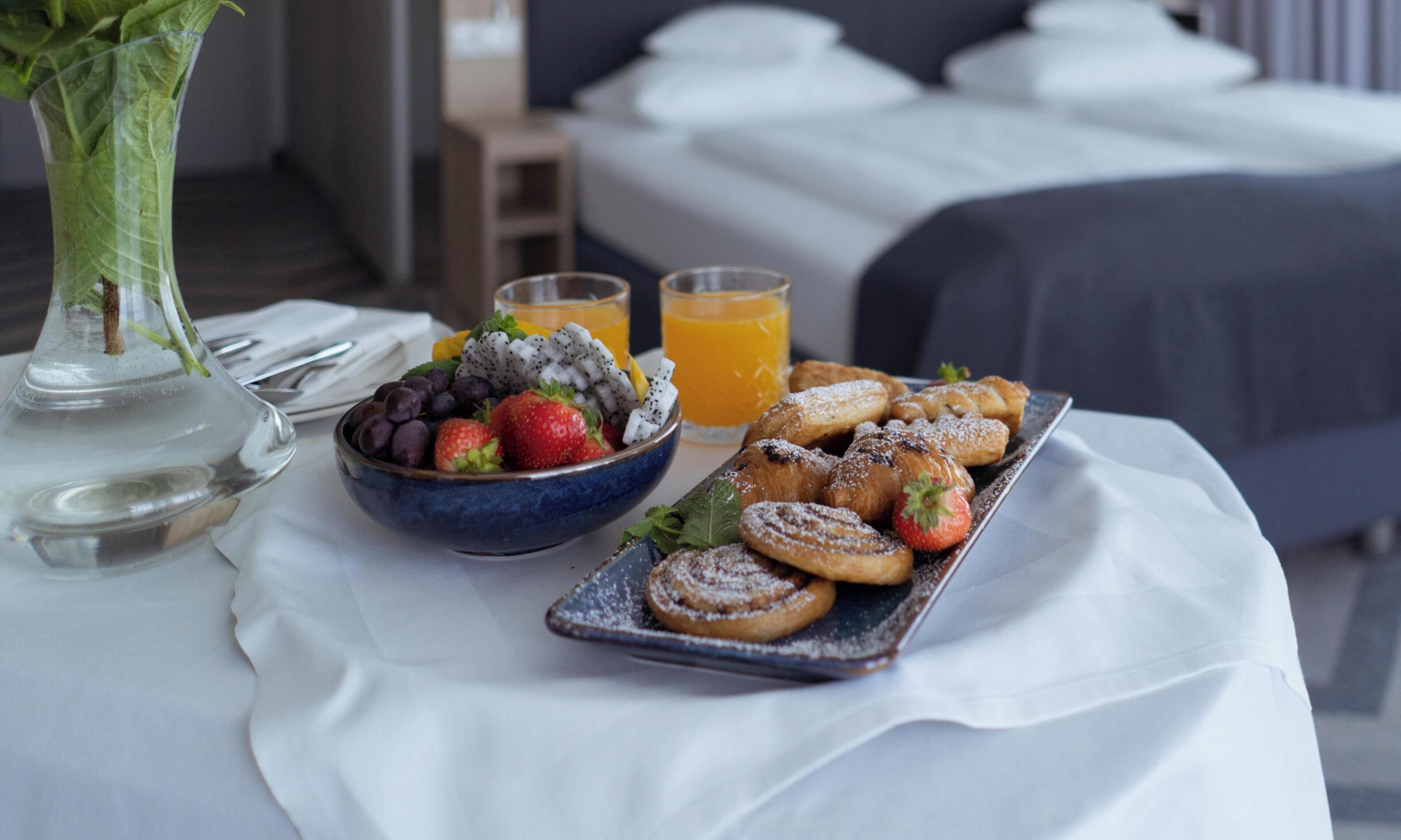 A breakfast table with a bowl of fruit, pastries, and two glasses of orange juice.