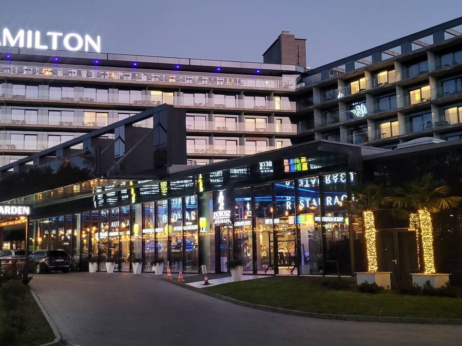 A modern hotel with a prominent "Hamilton" sign, a glass facade, and a well-lit entrance area.