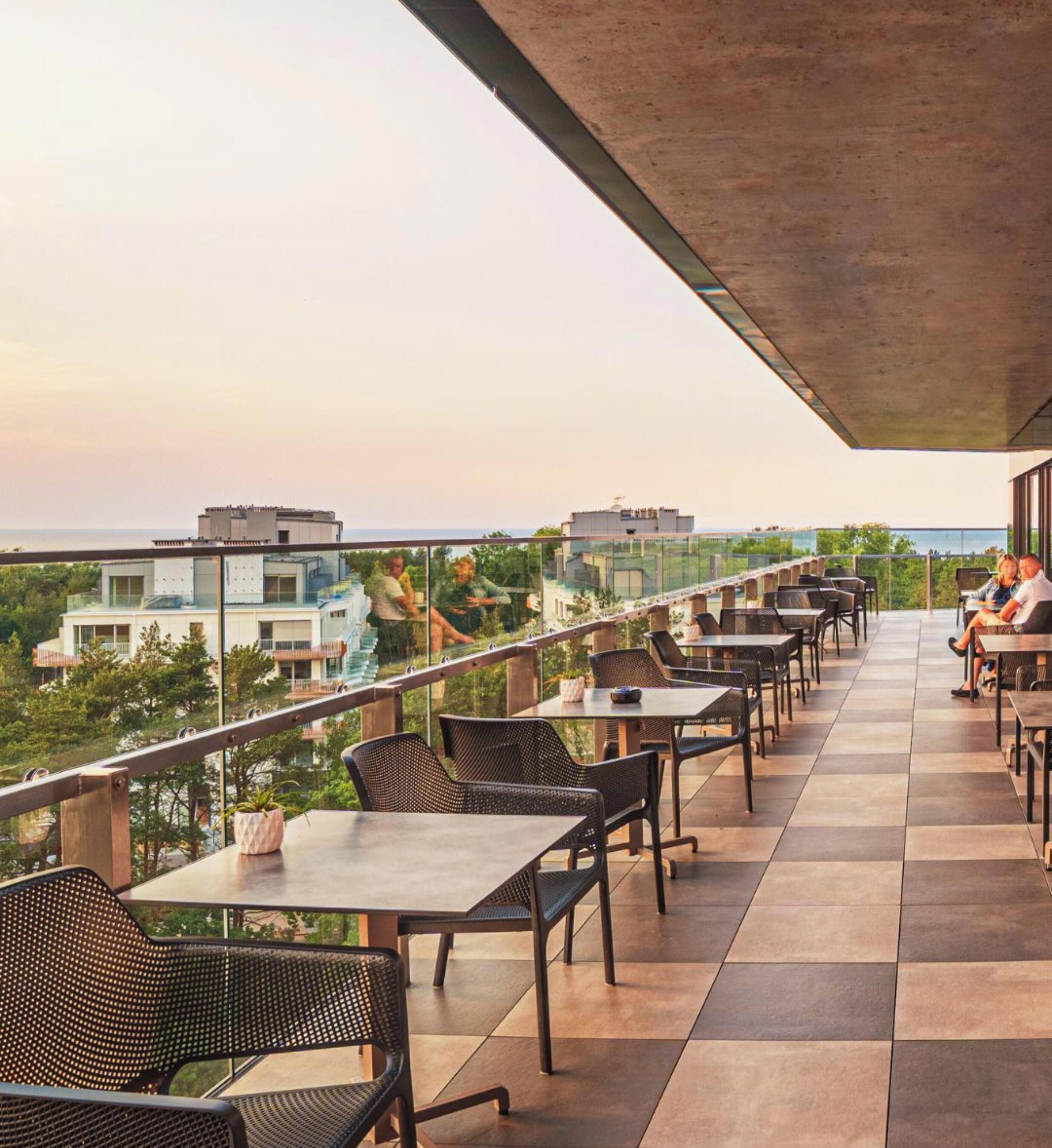 Una terraza al aire libre con mesas y sillas, con vistas a un paisaje urbano y zonas verdes.