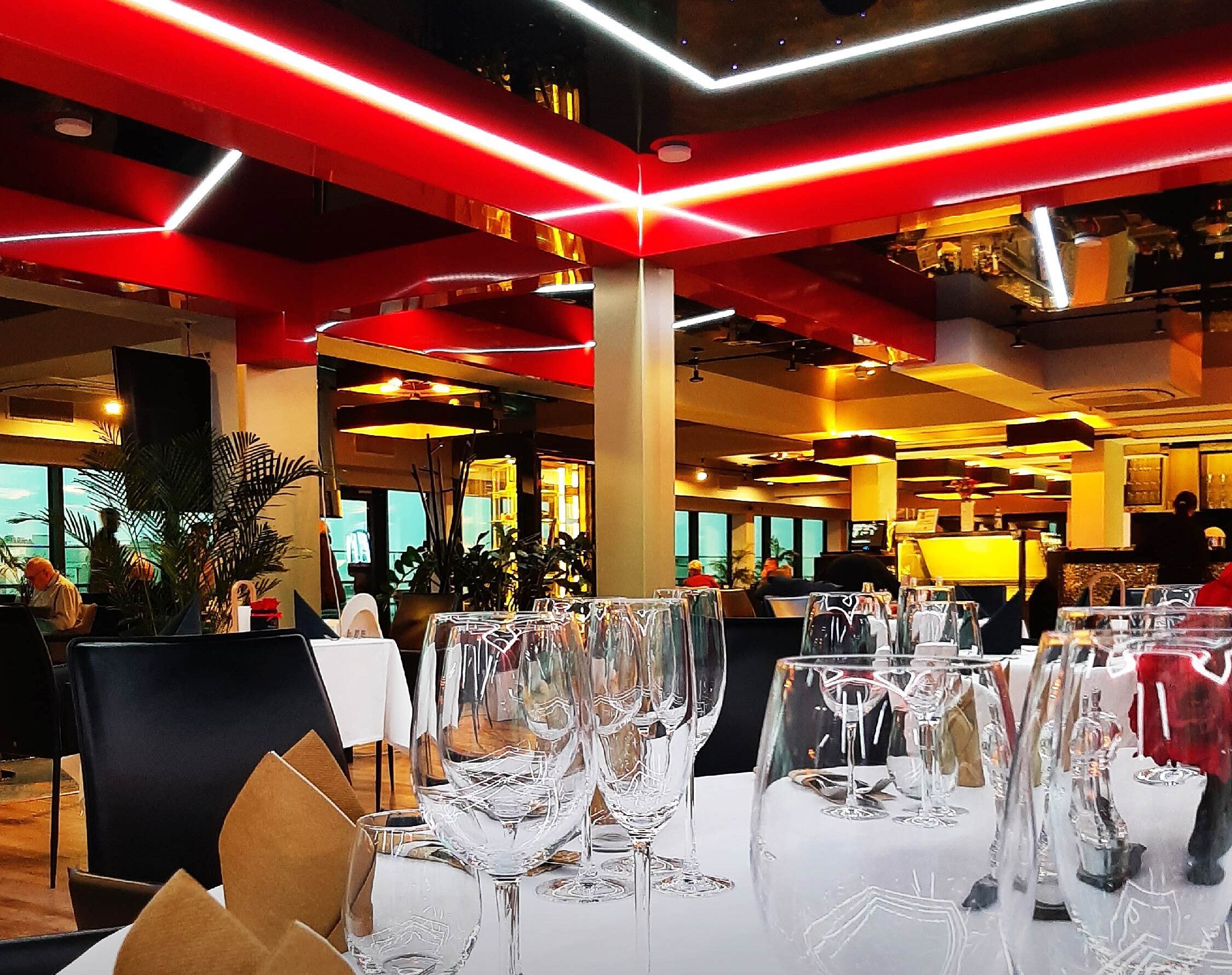 Un restaurante con mesas dispuestas para comer, con vasos transparentes y manteles blancos.