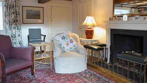 A cozy living room with a fireplace, a white armchair, a blue armchair, a small table with a lamp, and a patterned rug. - 3 bedroom accommodation in Rievaulx, near Helmsley (Rievaulx, near Helmsley)