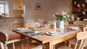 A dining area with a wooden table set for four, surrounded by chairs. There is a vase with flowers on the table, and a kitchen area is visible in the background. - 3 bedroom accommodation in Rievaulx, near Helmsley (Rievaulx, near Helmsley)