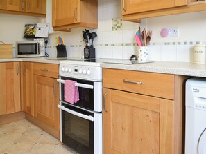 A kitchen with wooden cabinets, a microwave, a Beko oven, and a dishwasher.