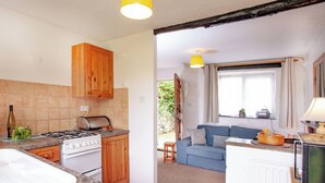 A compact kitchen with wooden cabinets, a gas stove, and a toaster. A blue sofa and a small table are visible in the adjacent living area. - 1 bedroom accommodation in Looe (Looe)