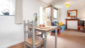 A cozy living room with a wooden dining table, a blue sofa, and a fireplace. - 1 bedroom accommodation in Looe (Looe)