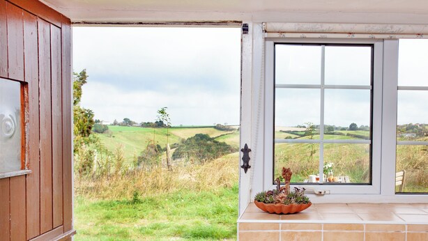 A bathroom with a view of a green landscape, a wooden door, and a tiled wall. - 1 bedroom accommodation in Looe (Looe)