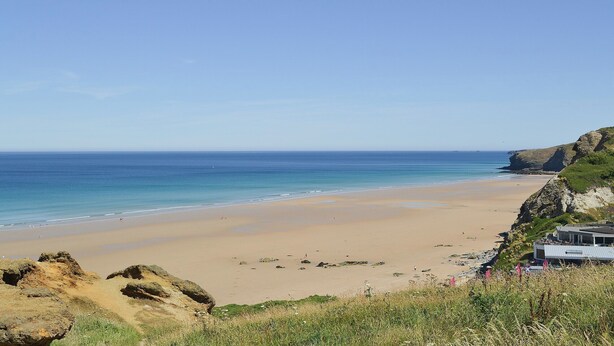 Une plage offrant une vue dégagée sur l’océan, une rive sablonneuse et un bâtiment doté d’un toit plat situé près du bord de l’eau.