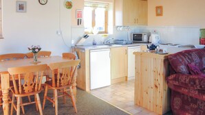 Une cuisine avec des meubles en bois, un four à micro-ondes et un évier. On y trouve une table à manger avec des chaises et un vase de fleurs.