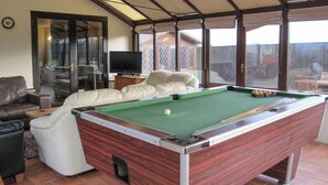 A pool table in a room with a sofa, a television, and a view through large windows. - 4 bedroom accommodation in Dumpling Green, near Dereham (Dumpling Green, near Dereham)