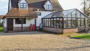 A two-story house with a large glass conservatory and a gravel driveway. - 4 bedroom accommodation in Dumpling Green, near Dereham (Dumpling Green, near Dereham)